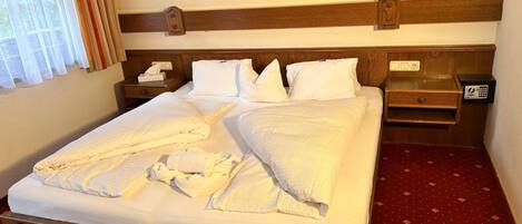 A hotel room with a neatly made bed, a bedside table with a lamp, a nightstand, and a wall-mounted TV.
