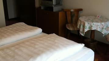 A hotel room with two beds, a television on a wooden stand, a small table with a floral tablecloth, and a wicker basket.