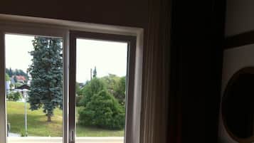 A hotel room with a bed, a desk, a lamp, and a view through a sliding door to a street and greenery.