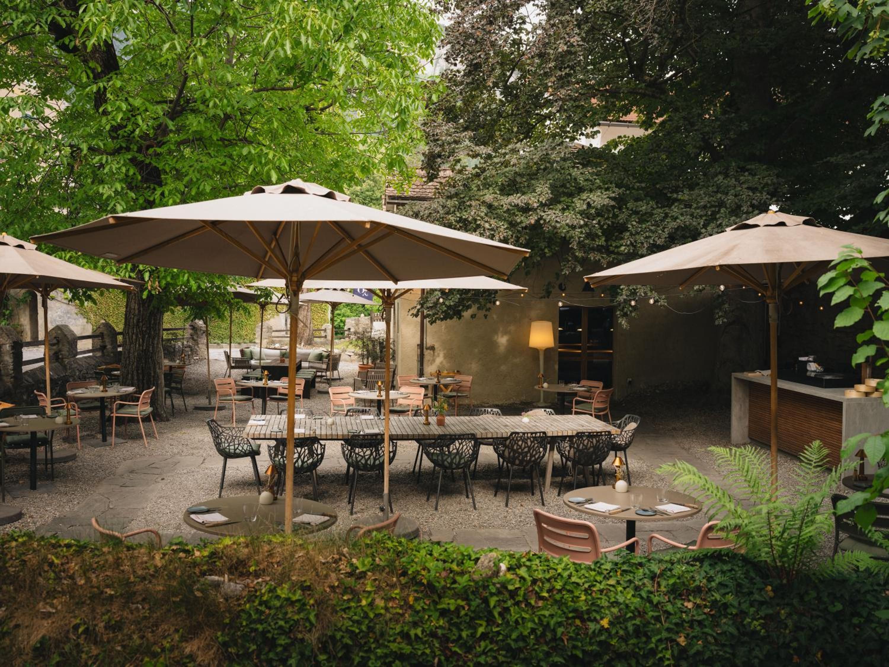 An outdoor patio area with tables and chairs, surrounded by greenery and trees.