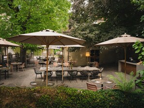 An outdoor patio area with tables and chairs, surrounded by greenery and trees.