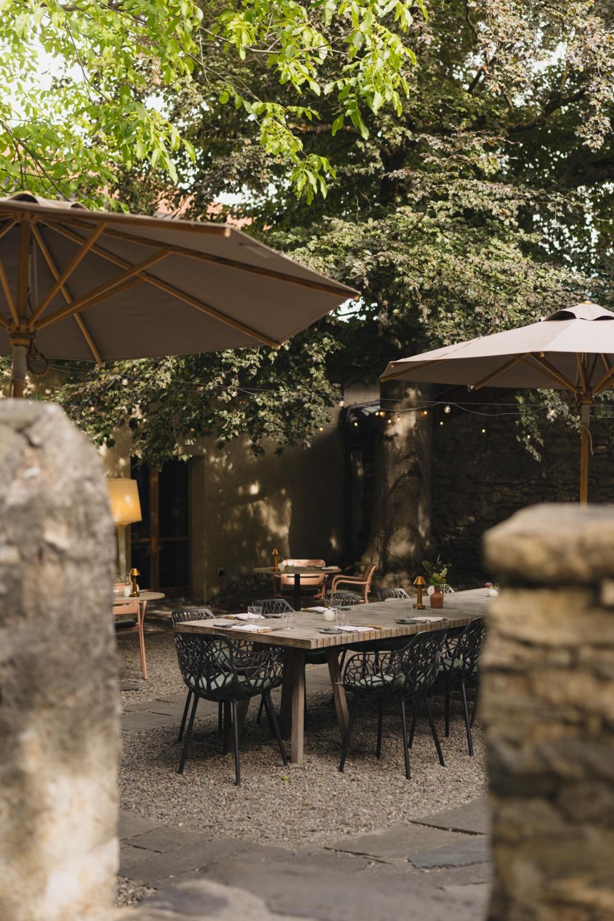 An outdoor patio area with a table and chairs, surrounded by stone walls and covered by umbrellas.