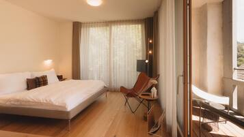 Ein Schlafzimmer mit einem großen Bett, einem Sessel, einem Balkon mit Geländer und einem Fenster mit Vorhängen.