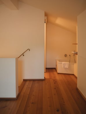 A room with a wooden floor, a bathtub, and a white wall.