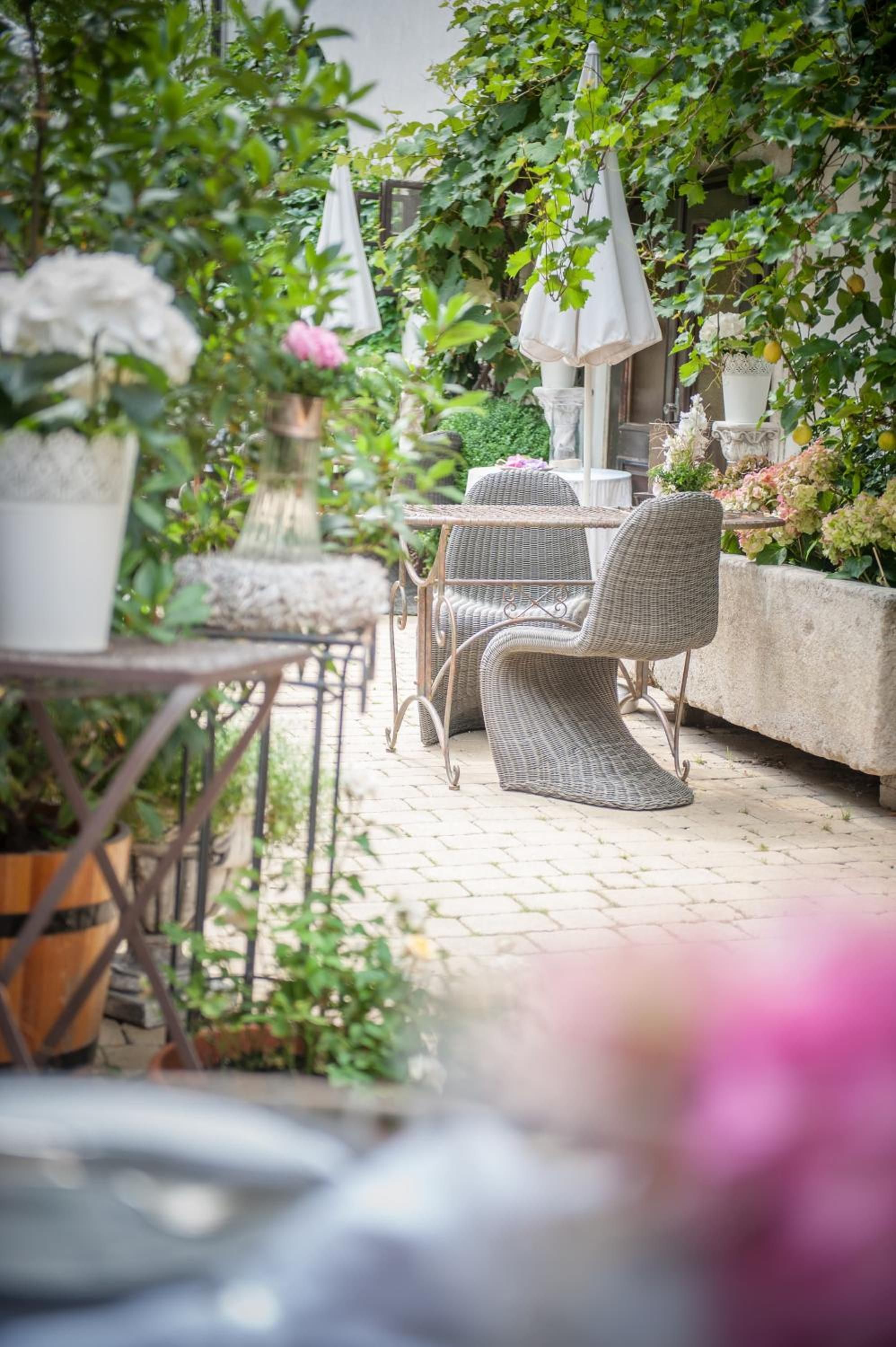 An outdoor patio with wicker furniture, potted plants, and a stone wall.