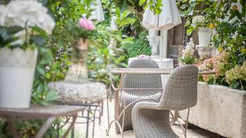 An outdoor patio with wicker furniture, potted plants, and a stone wall.