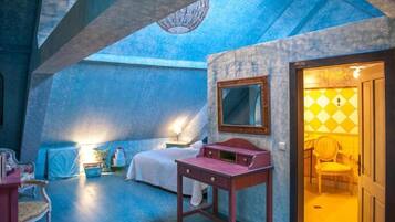 A bedroom with a bed, bedside table, and a mirror. There is a door leading to another room.