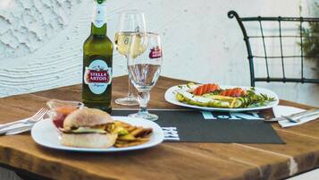 Ein Holztisch mit einer Stella Artois Bierflasche, einem Glas Weißwein, einem Sandwich und einer Salatplatte.