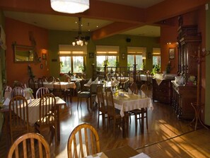 A dining area with multiple tables and chairs, large windows, and a chandelier. - Hotel Kochanv W (Zabierzow)