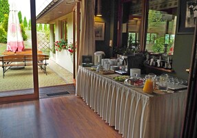 A breakfast buffet setup with a table covered in a tablecloth, various food items, and a coffee machine.