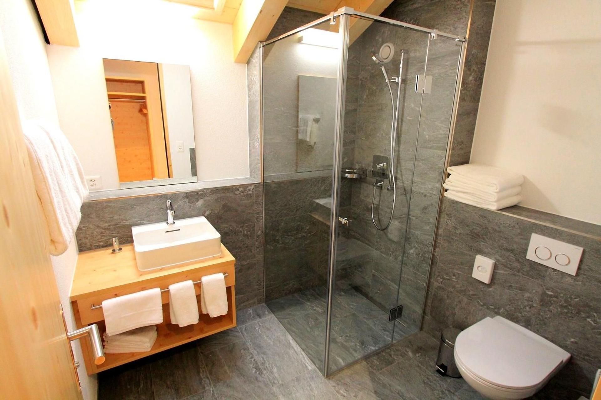 Ein modernes Badezimmer mit einer Duschkabine, einem Holzwaschtisch und einer Toilette.