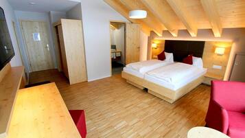 Ein Schlafzimmer mit Holzboden, einem Bett mit weißer Bettwäsche, einem roten Sessel und einer Holzbalkendecke.