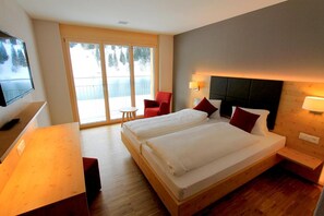 A hotel room with two beds, a TV, a desk, and a balcony with a view. - Hotel Espen (Engelberg)