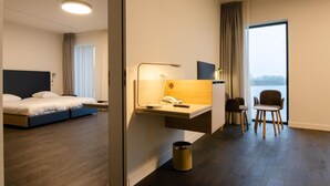 A hotel room with a bed, desk, chair, and a view of a body of water. - Domein Polderwind (Zuienkerke)