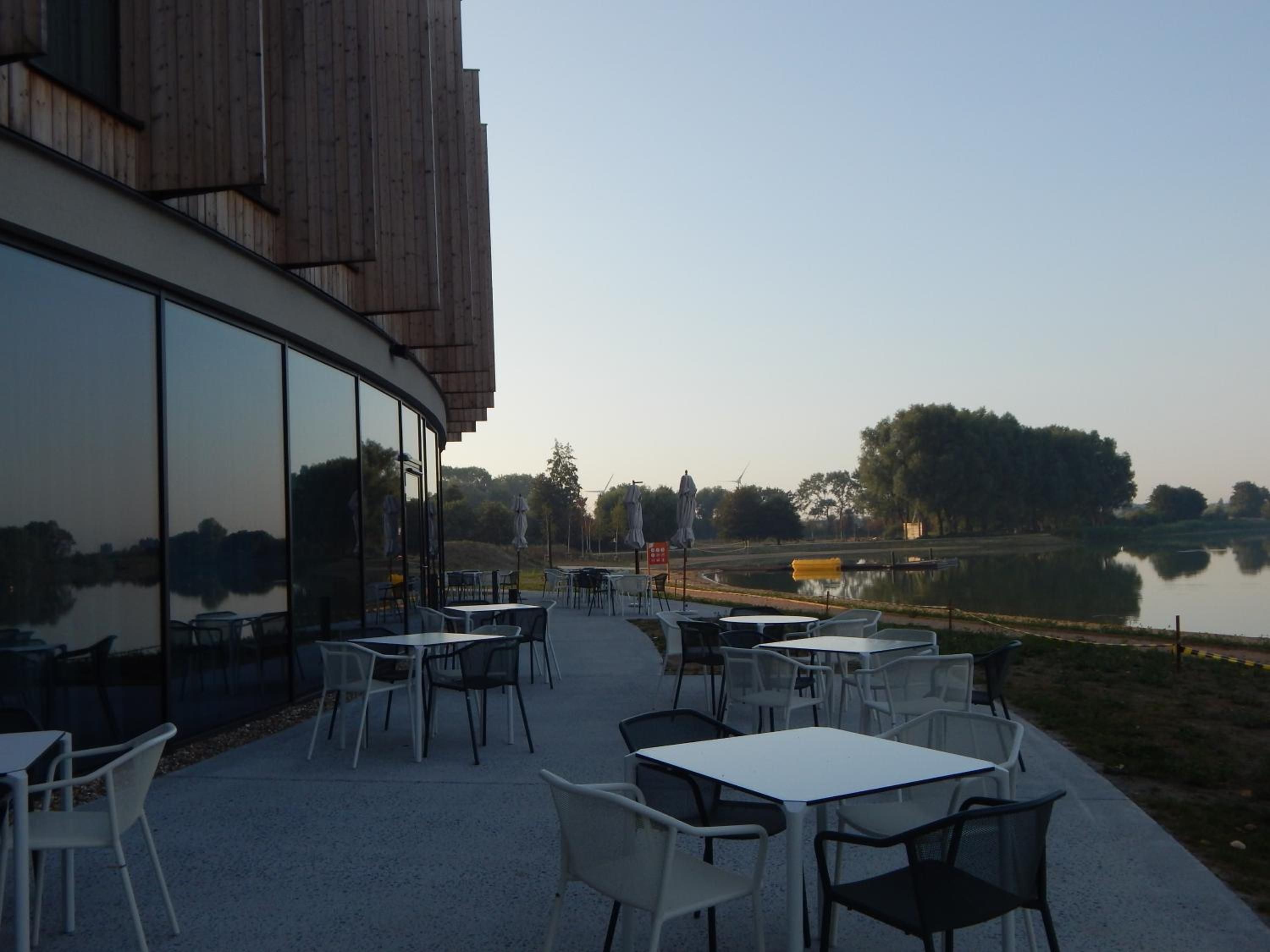 An outdoor seating area with tables and chairs, overlooking a body of water and trees.