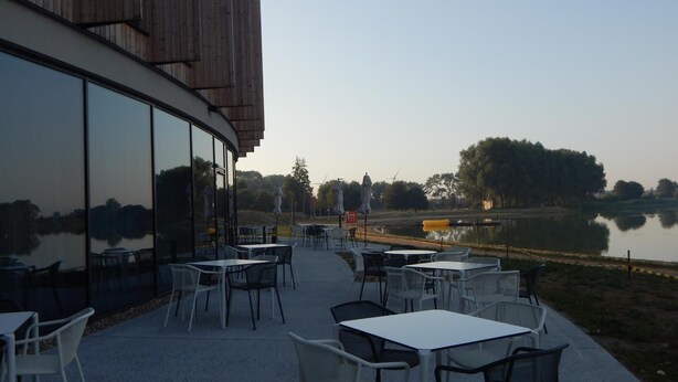 An outdoor seating area with tables and chairs, overlooking a body of water and trees. - Domein Polderwind (Zuienkerke)
