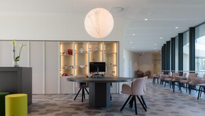 A modern interior with a round table, chairs, a yellow stool, and a large window. - Domein Polderwind (Zuienkerke)