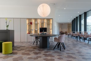 A modern interior with a round table, chairs, a yellow stool, and a large window. - Domein Polderwind (Zuienkerke)