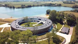 A circular building with a central courtyard, surrounded by a lake and greenery. - Domein Polderwind (Zuienkerke)