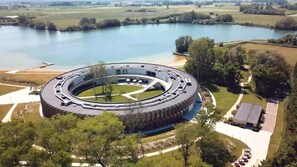A circular building with a central courtyard, surrounded by a lake and greenery. - Domein Polderwind (Zuienkerke)