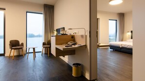 A hotel room with a desk, two chairs, a bed, and a view of the outdoors. - Domein Polderwind (Zuienkerke)