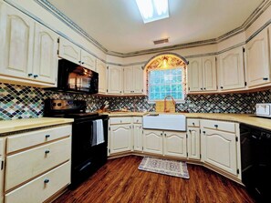 A kitchen with white cabinetry, a black stove, a window with a view, and a patterned backsplash. - Casa del Verde - a DZ Collection (Foley)