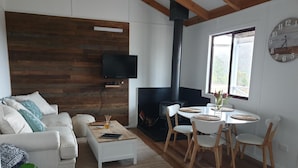Een moderne woonkamer met een witte bank, een salontafel, een open haard, een eethoek met stoelen en een aan de muur bevestigde televisie.