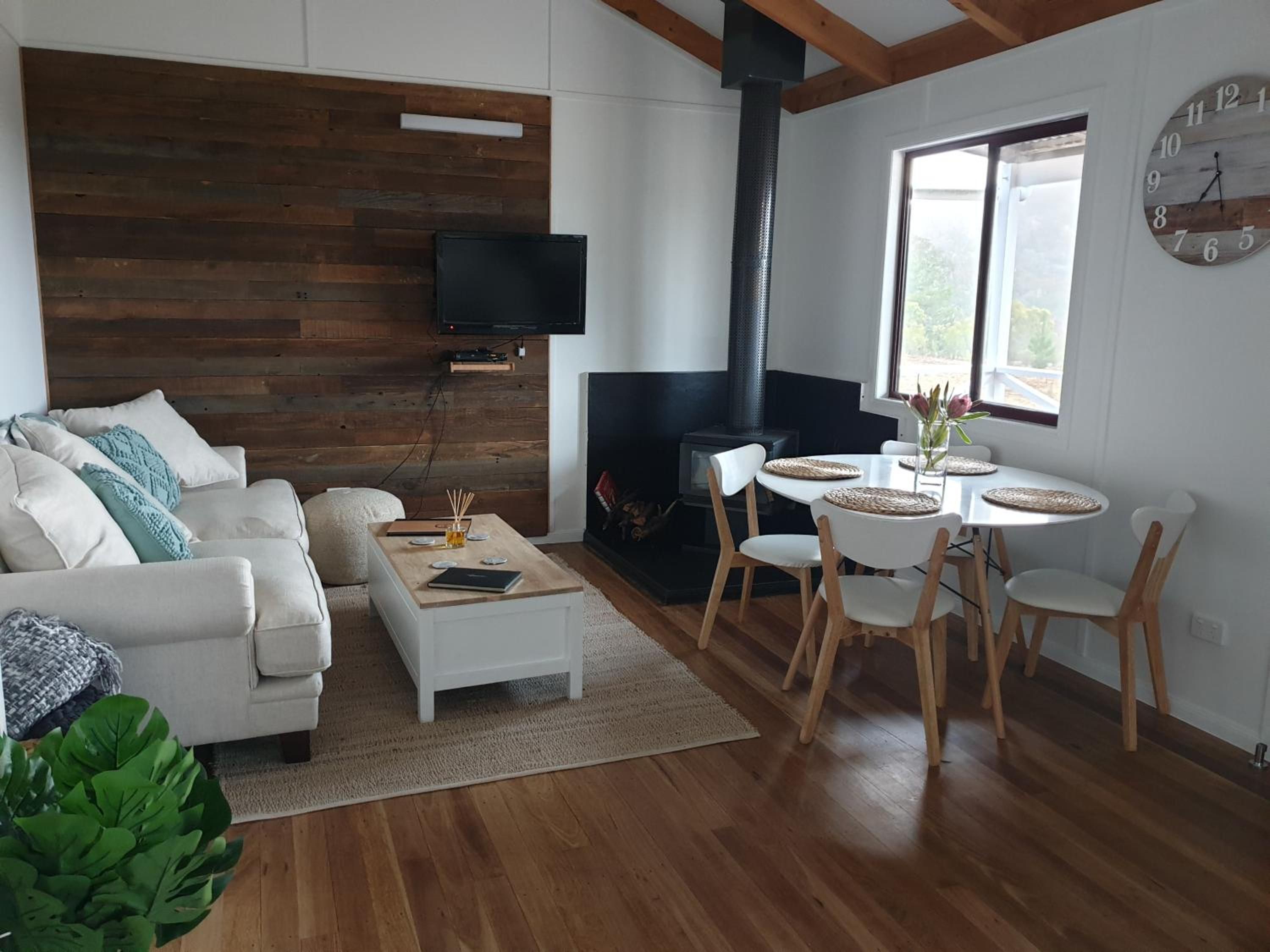 A modern living room with a white sofa, a coffee table, a fireplace, a dining area with chairs, and a wall-mounted TV.