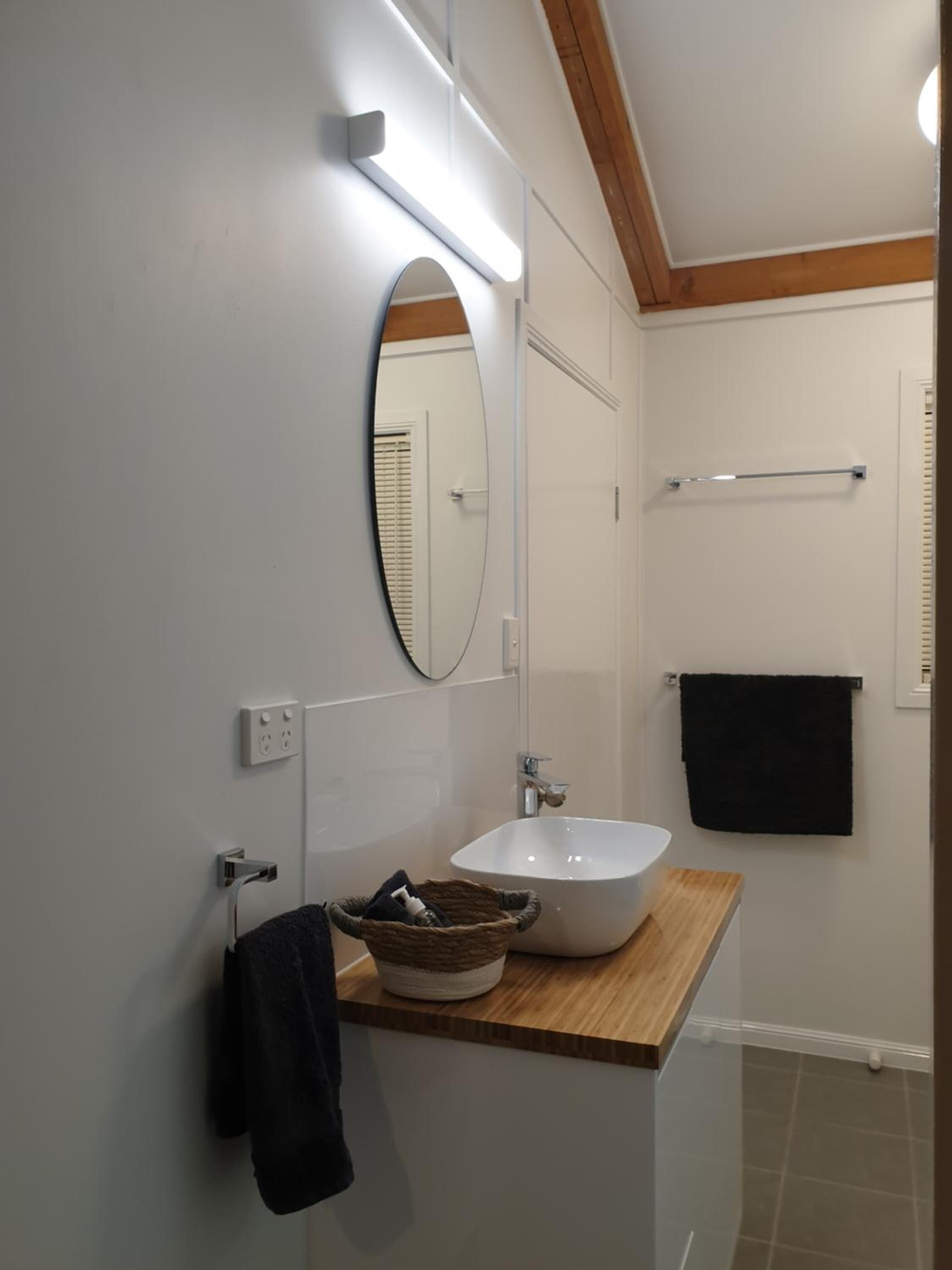 A bathroom with a wooden vanity, a white sink, a mirror, and a towel rack.