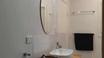 A bathroom with a wooden vanity, a white sink, a mirror, and a towel rack.