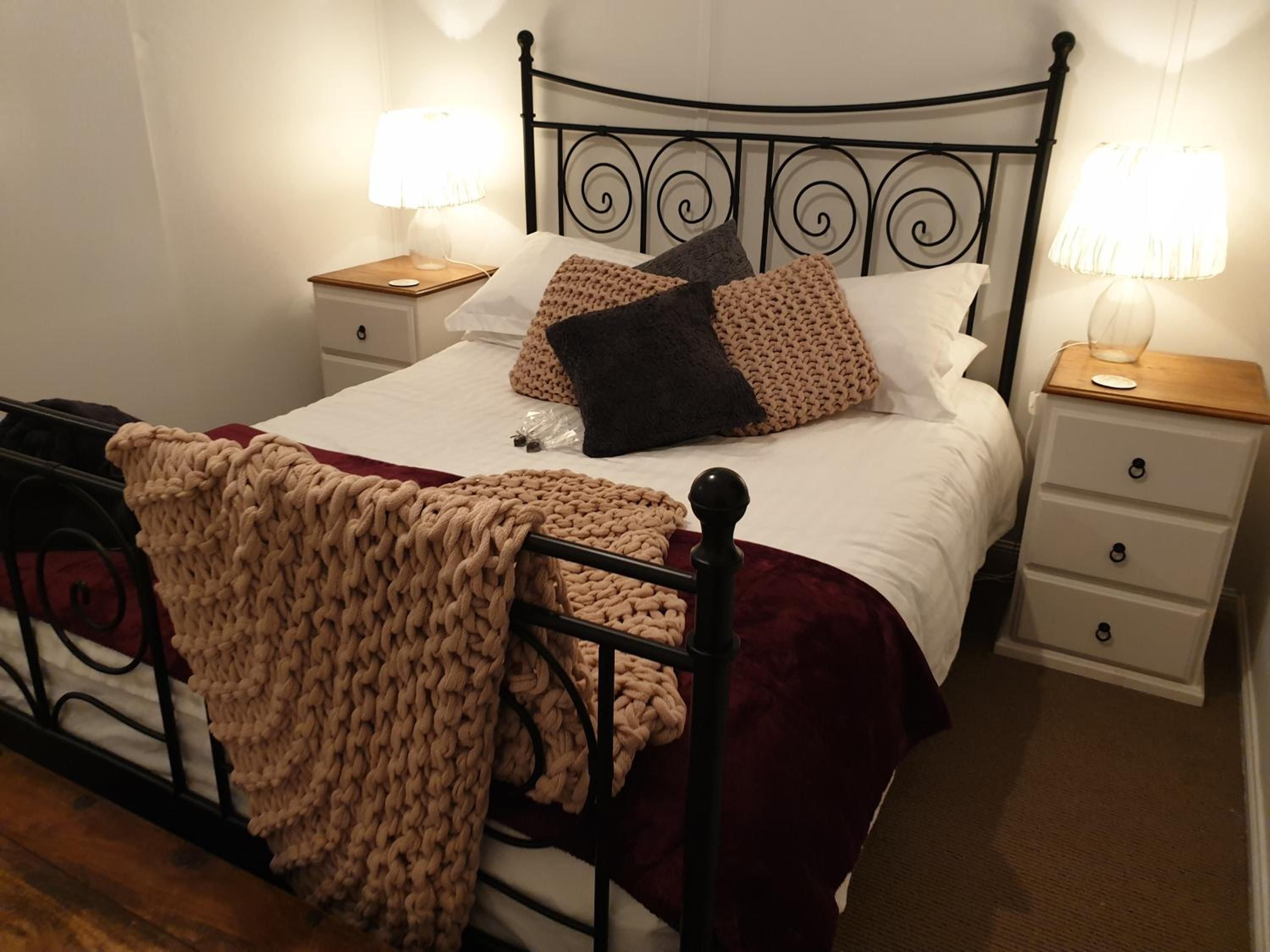 A neatly made bed with a knitted blanket, two bedside tables with lamps, and a wooden nightstand.