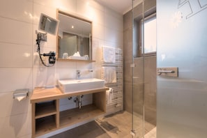 Un baño moderno con tocador de madera, un espejo grande, un calentador integrado y un box de ducha de vidrio.
