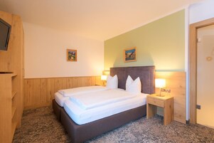 Una habitación de hotel con una cama, mesitas de noche y un televisor sobre un mueble de madera.