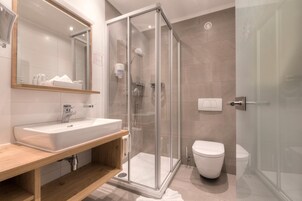 Un baño moderno con ducha envuelta en vidrio, un lavamanos blanco y un inodoro.