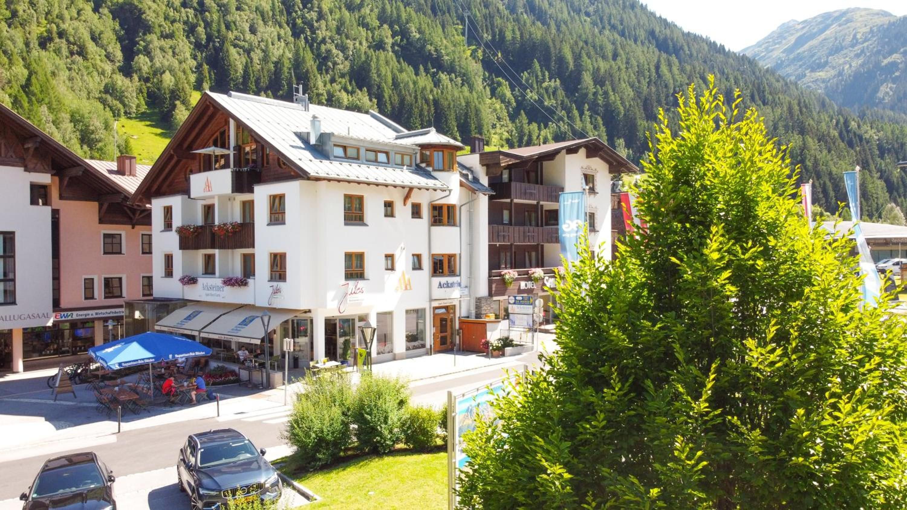 Un hotel con varios pisos, balcones y un paisaje de montañas al fondo.