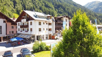 Un hotel con varios pisos, balcones y un paisaje de montañas al fondo.