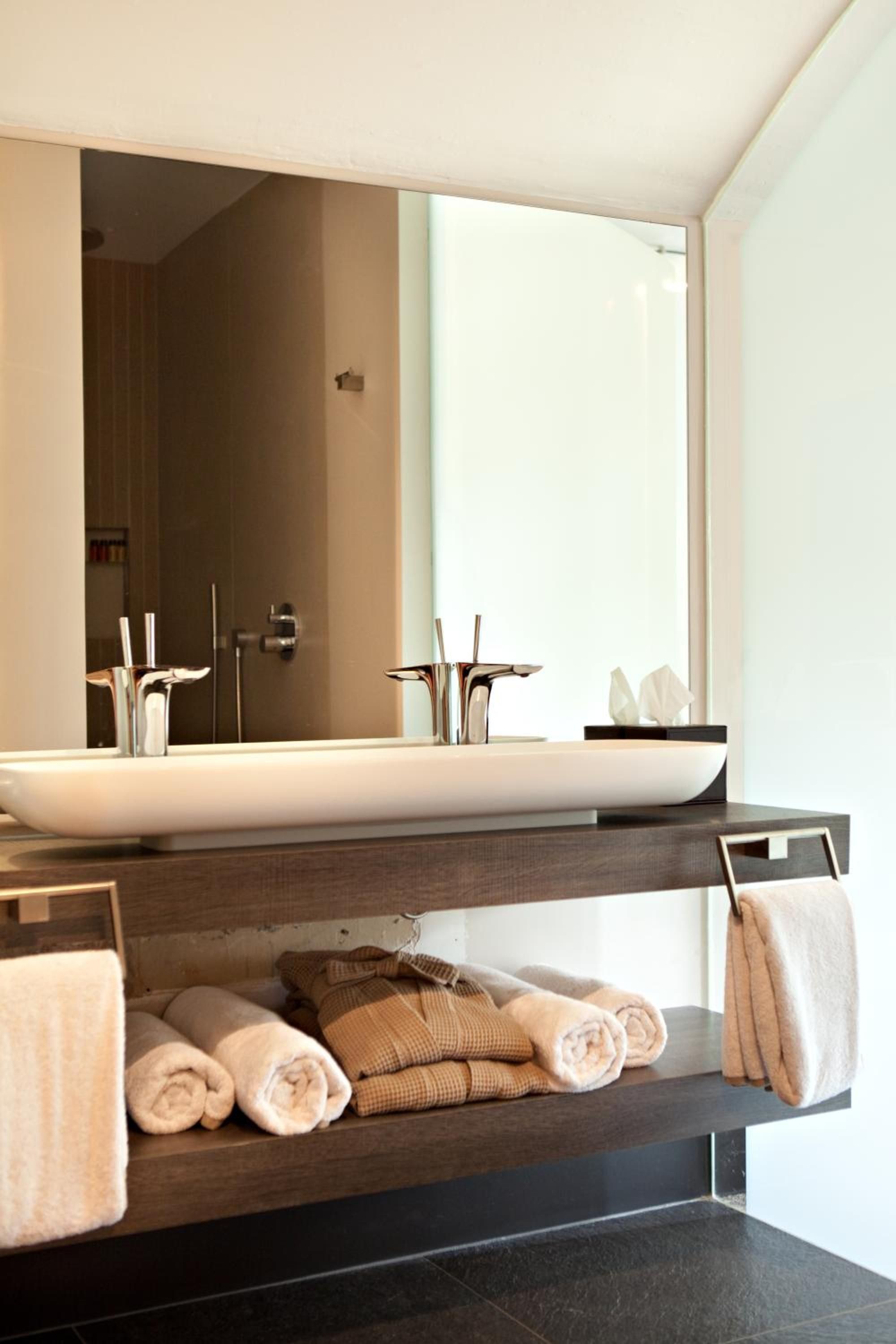 A modern bathroom with a large mirror, a white sink, and neatly folded towels on a shelf.