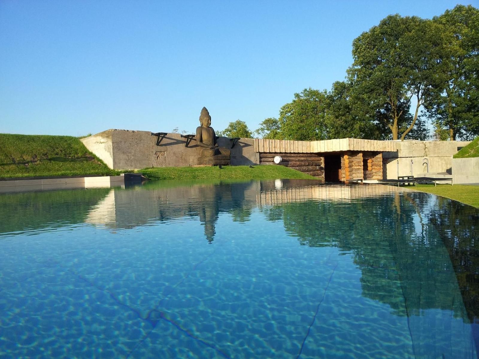 A clear pool with a Buddha statue, a stone wall, and a wooden bridge.