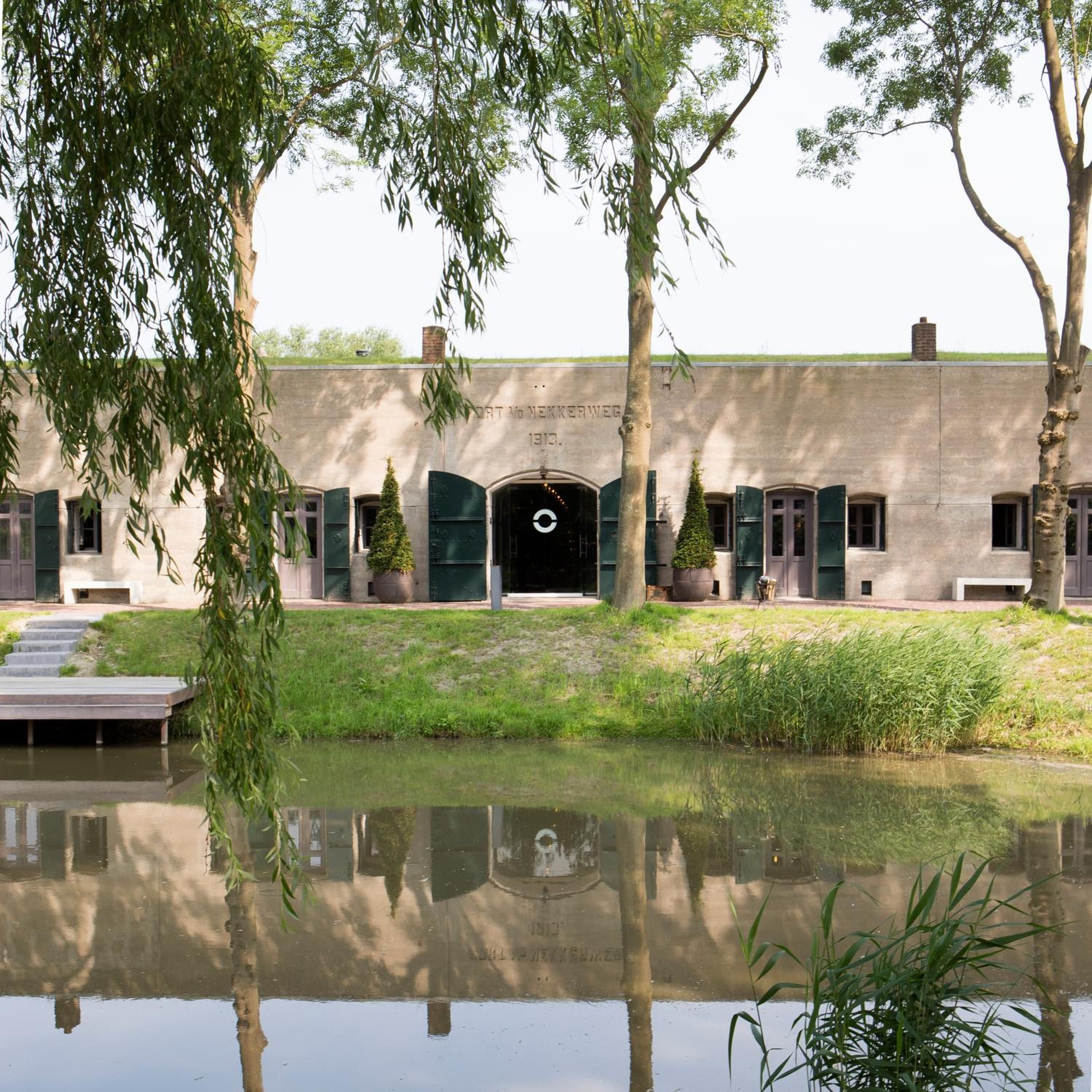 A building with a water body in front, a paved pathway, and a gate.
