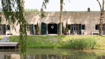 A building with a water body in front, a paved pathway, and a gate.