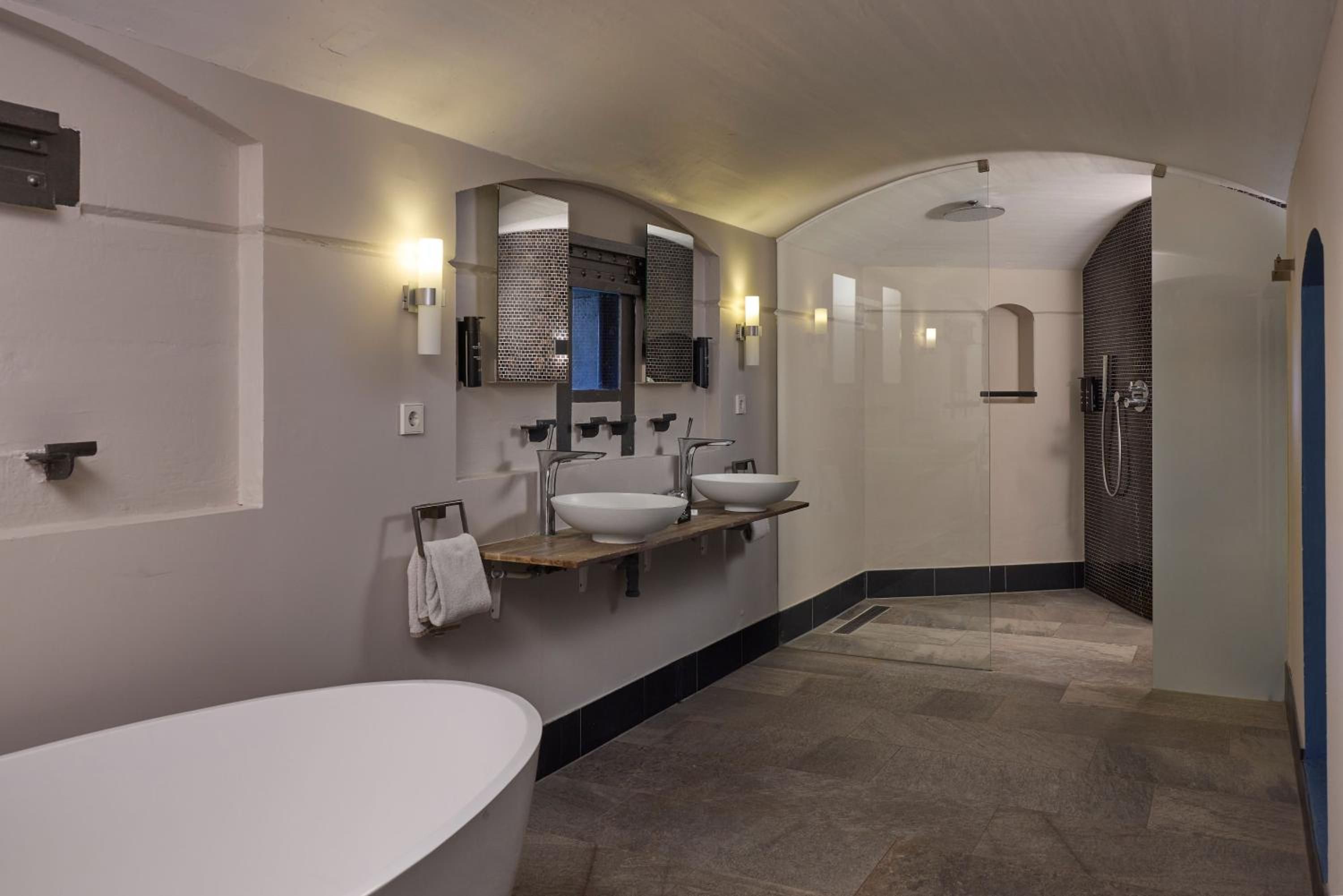 A modern bathroom with a large bathtub, two sinks, and a shower area.