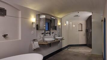 A modern bathroom with a large bathtub, two sinks, and a shower area.