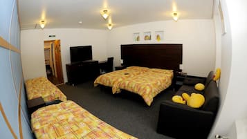 Habitación de hotel con dos camas individuales, una cama doble, televisión, escritorio y una silla.