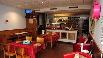 Ein Restaurant mit Holztischen und -stühlen, einer Bar mit Flaschen und einem Fernseher an der Wand.