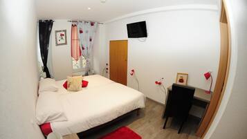 Ein Schlafzimmer mit einem Bett, einem Schreibtisch, einem Stuhl, einem Fernseher und einer Tür.