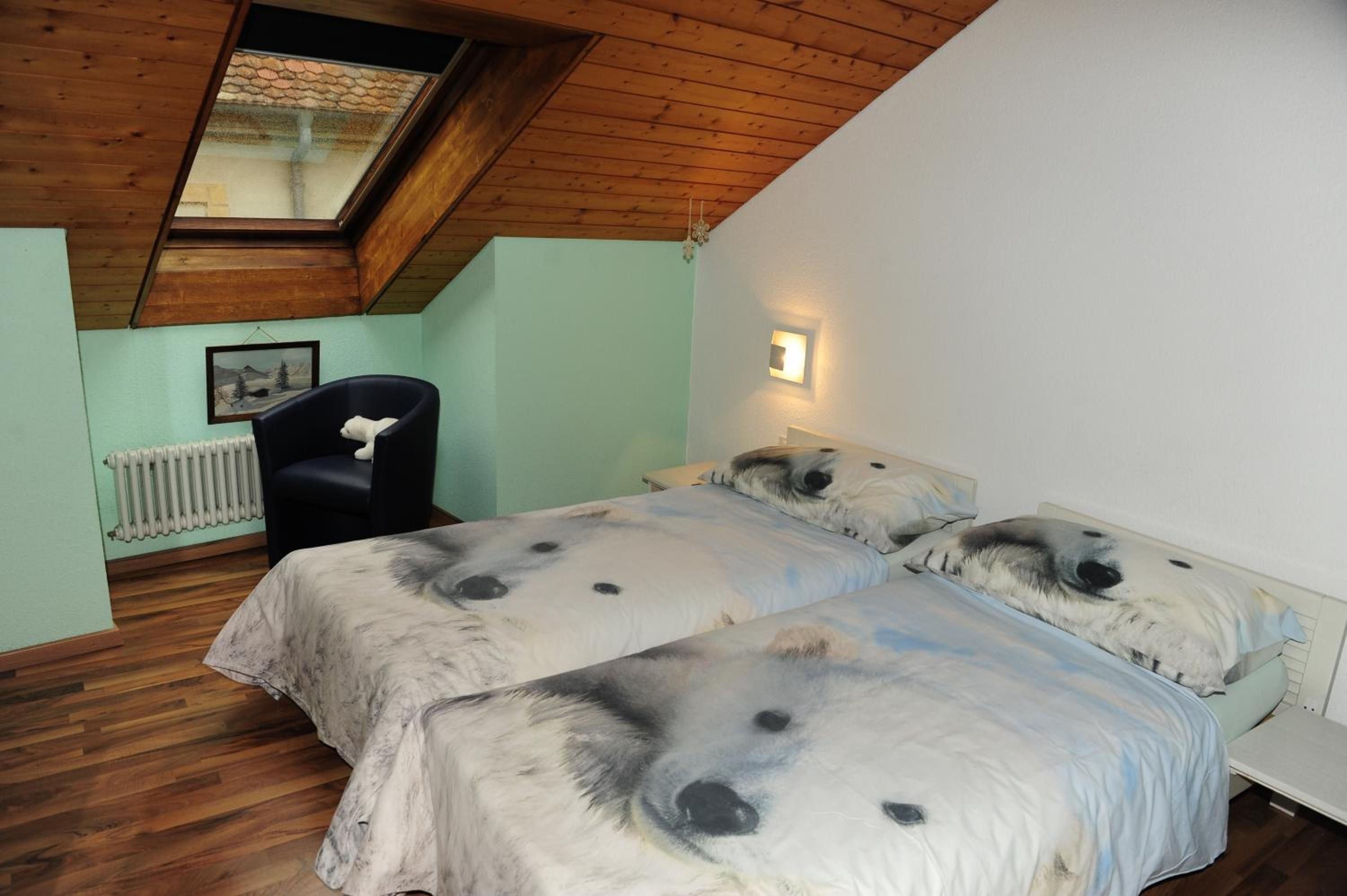 Quarto com teto inclinado, radiador, cadeira e cama com estampa de urso polar.