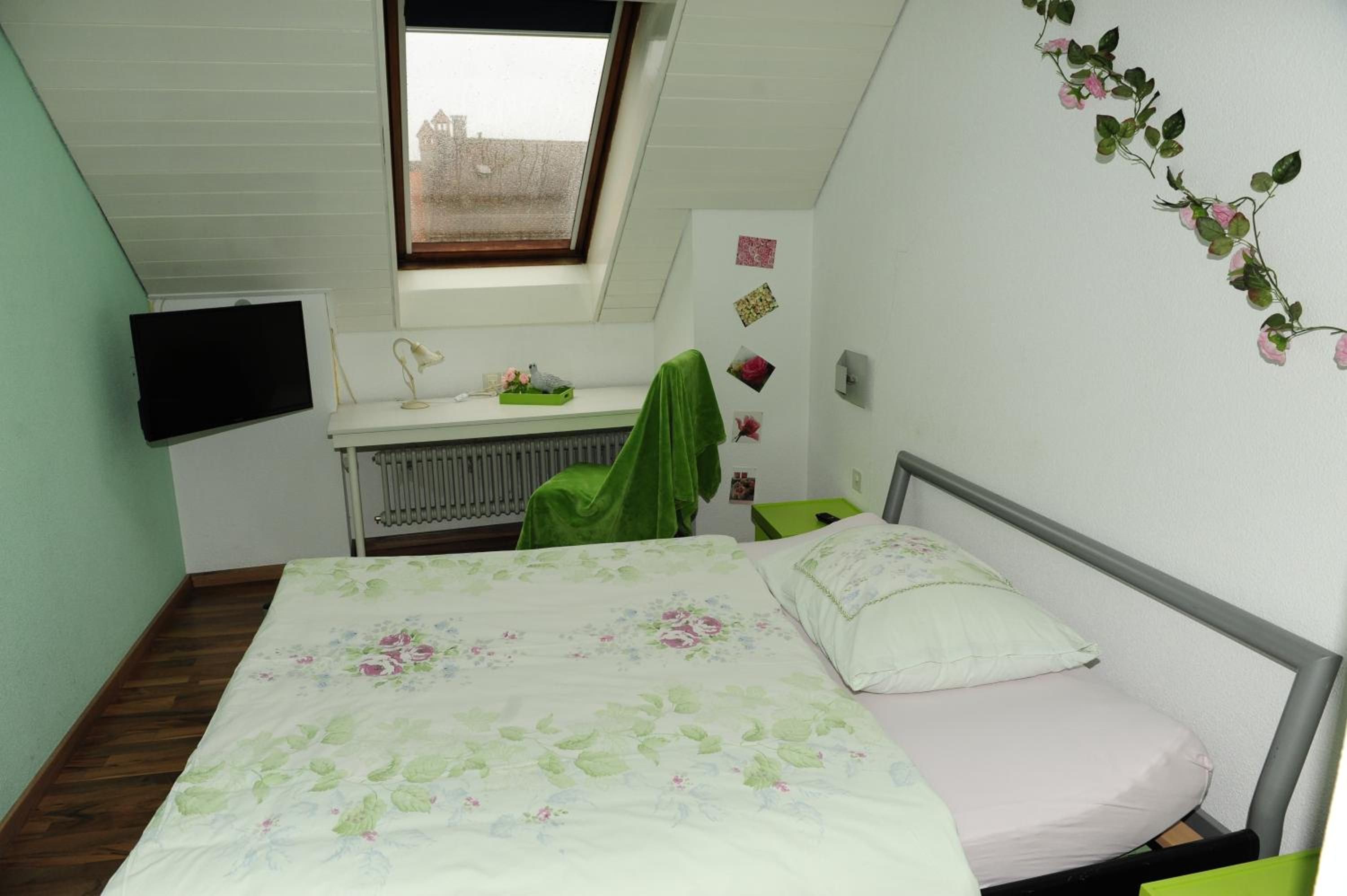 A bedroom with a bed, a desk, a radiator, a window, and a wall decoration.