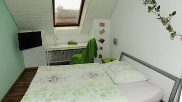 A bedroom with a bed, a desk, a radiator, a window, and a wall decoration.
