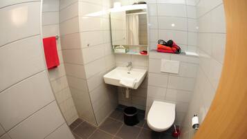 A small bathroom with a white sink, a toilet, and a shower area.