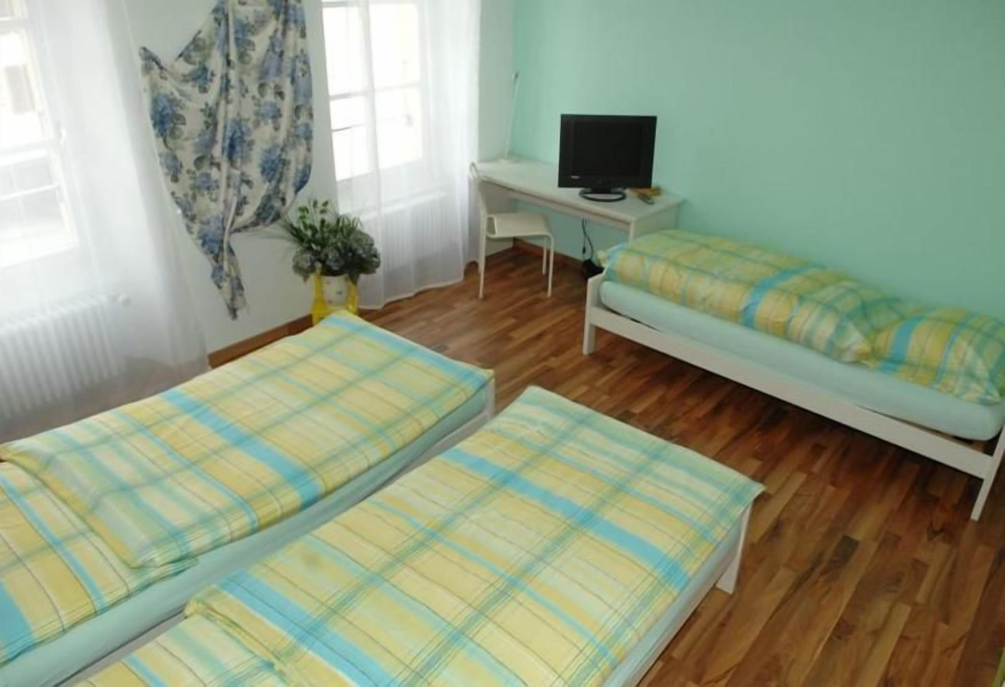 A room with two beds, a desk with a computer, and a window with curtains.